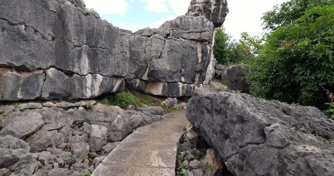 First person perspective walking along winding stone path closely flanked by massive weathered karst limestone walls and rugged boulders in Shilin Stone Forest.