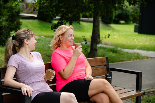 Friends sit on a bench in a park talking and enjoying drinks on a sunny day