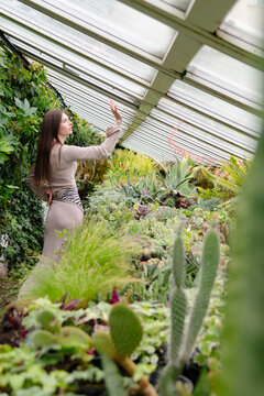 Woman standing in a greenhouse surrounded by various plants and cacti during daytime