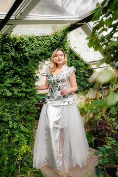 A woman poses in a greenhouse surrounded by plants