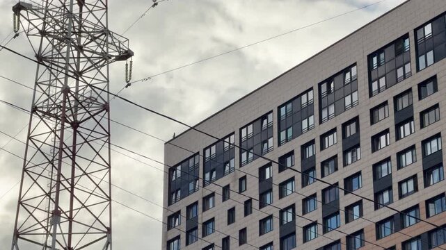 A high metal tower stands near a modern apartment building in Saint Petersburg. Power lines cross the cloudy sky above. The quiet city scene evokes a calm and serious mood.