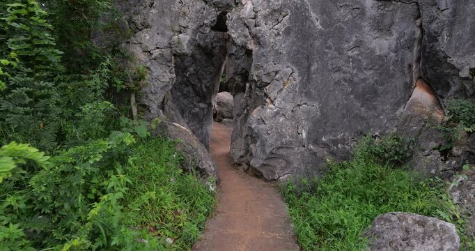 Immersive first-person perspective walking through natural karst portal and following winding stone path in Shilin Stone Forest. POV shot captures experience of squeezing through narrow passage