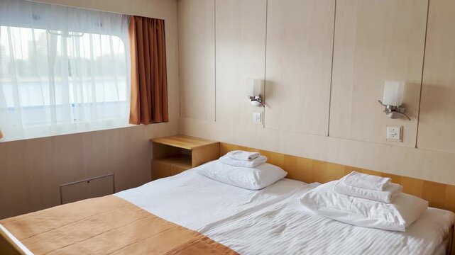 A cozy bed rests in a neat cruise ship cabin on the Neva River. Soft light shines through the window, creating a peaceful atmosphere. The quiet room offers a feeling of warm comfort.