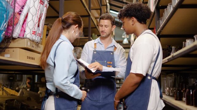 Diverse team of retail workers in blue aprons discussing inventory management. Manager with clipboard talking to warehouse staff in store storage room. Small business teamwork and logistics concept.