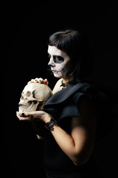 Day of the Dead or Halloween themed image with a woman with skull painting on her face and a skull.	