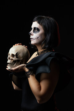 Day of the Dead or Halloween themed image with a woman with skull painting on her face and a skull.	