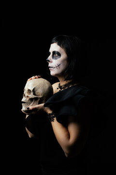 Day of the Dead or Halloween themed image with a woman with skull painting on her face and a skull.	