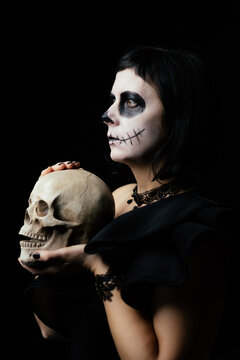 Day of the Dead or Halloween themed image with a woman with skull painting on her face and a skull.	