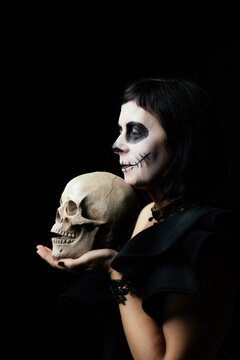 Day of the Dead or Halloween themed image with a woman with skull painting on her face and a skull.	