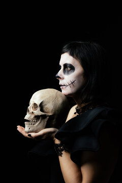 Day of the Dead or Halloween themed image with a woman with skull painting on her face and a skull.	