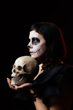 Day of the Dead or Halloween themed image with a woman with skull painting on her face and a skull.	