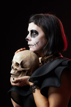 Day of the Dead or Halloween themed image with a woman with skull painting on her face and a skull.	