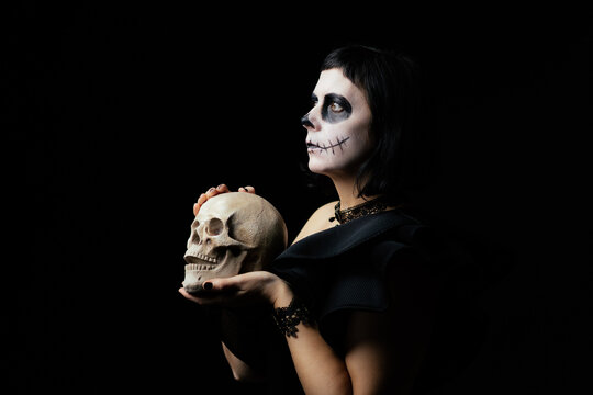 Day of the Dead or Halloween themed image with a woman with skull painting on her face and a skull.	