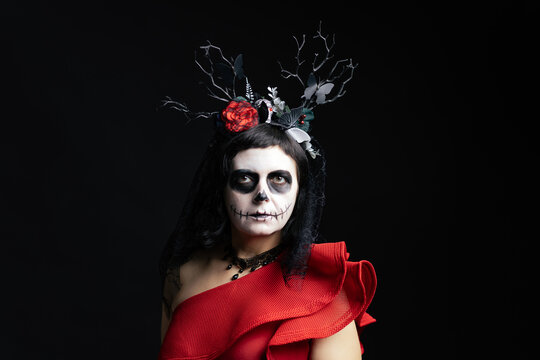 Day of the Dead or Halloween themed image with a woman with skull painting on her face and a skull.	