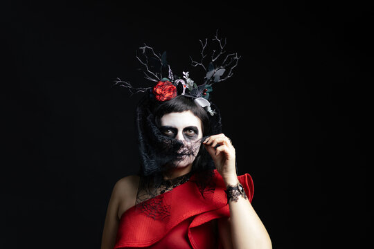 Day of the Dead or Halloween themed image with a woman with skull painting on her face and a skull.	