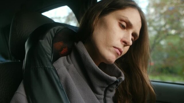 Young woman relieving neck and shoulder pain, sitting in car using electric shiatsu massager for relaxation, muscle ache relief, physical therapy after long drive. Woman using electric massager in car