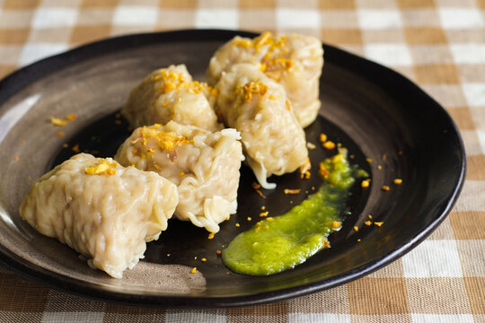 Homemade pork and shrimp shumai dim sum topped with fried garlic, served on a black plate with green chili sauce.