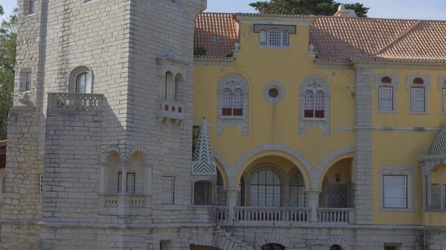 Turreted stone tower and yellow wing of the Condes de Castro Guimaraes Museum, a early twentieth century revivalist mansion on the seafront in Cascais, under a clear sky