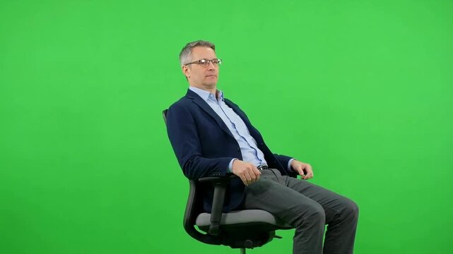 Professional middle-aged man wearing glasses and formal business attire, seated on an office chair against a bright green chroma key background