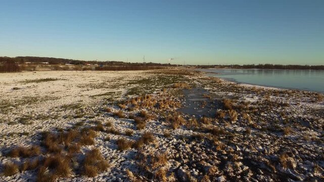 Snow-covered wetland and frozen Ega Engso lake wetland under clear winter sky near Aarhus, Denmark, aerial medium dolly above icy white area