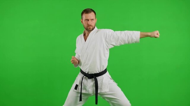 Martial artist in a white uniform performs a powerful side punch against a bright green chroma key background