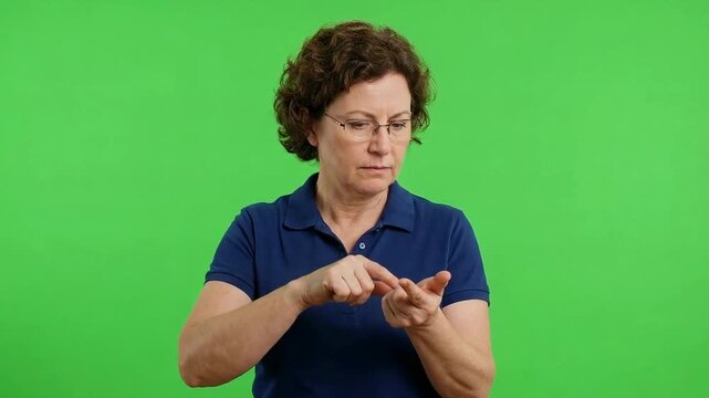 Middle-aged woman in a navy polo shirt demonstrates hand gestures and sign language against a bright green screen background