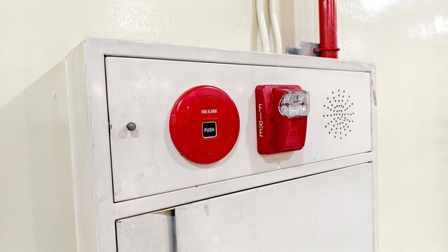 a close-up, angled view of a white, wall-mounted fire protection cabinet set against a light beige wall. The top section of the metal cabinet features integrated emergency equipment