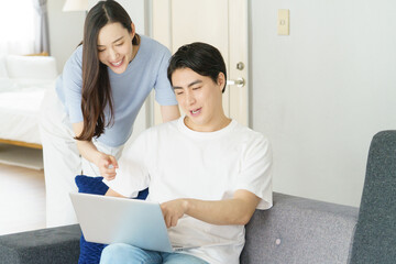 Fototapeta premium リビングのソファでノートパソコンを見る若い日本人のパワーカップル