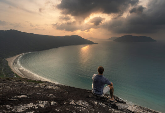 Solo male traveller observing a colorful sunrise from a viewpoint overlooking the bay and Dat Doc Beach on Con Son Island in the Con Dao archipelago, Vietnam