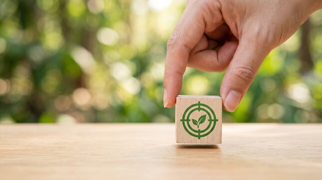 Human hand holding wooden block with green leaf target icon representing eco friendly business goals and sustainable growth strategy today