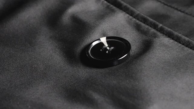 A close-up of a black satin trench coat with large round buttons, smooth waterproof fabric, neat seams, elegant classic outerwear details, and shiny elements on high-quality synthetic materia