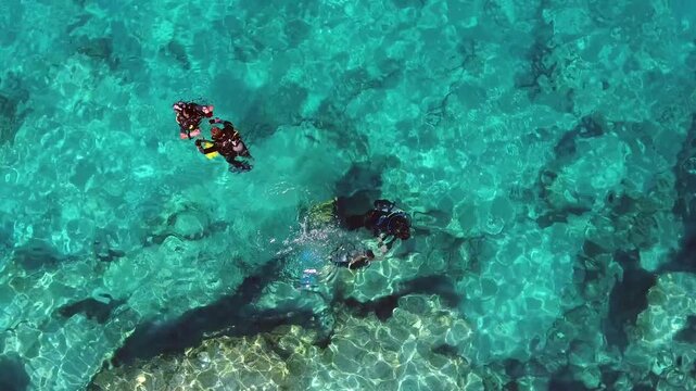 Aerial scuba diving training above rocky reef shows students and instructors in clear blue sea.