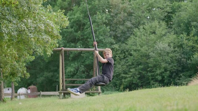 The boy is riding on a zip line swing slow motion outdoors