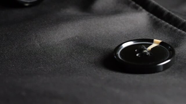 A close-up of a black satin trench coat with large round buttons, smooth waterproof fabric, neat seams, elegant classic outerwear details, and shiny elements on high-quality synthetic materia