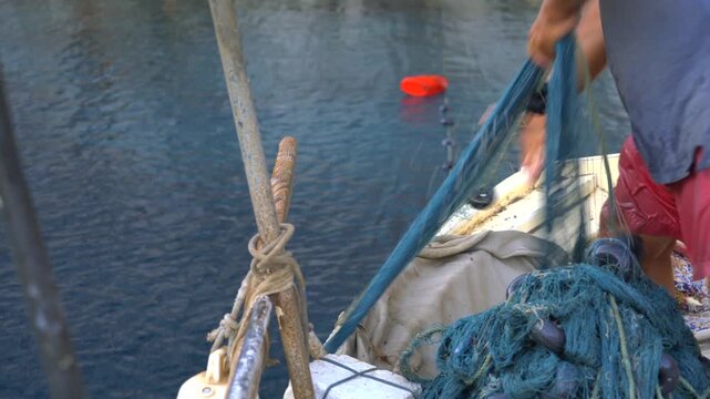 Fisherman hauls a fishing net by hand into a small boat on open water in natural habitat.