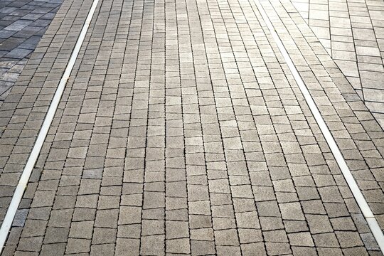 High-angle shot of gray paving block street with integrated narrow parallel tracks or design lines in modern urban pedestrian area.