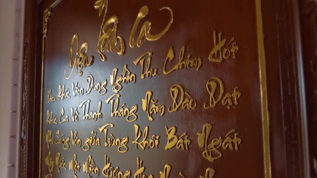 A close-up of a traditional Vietnamese calligraphy art piece, likely featuring gilded lettering on a dark, polished wood or lacquer background situated in Hai Duc Buddhist Institute