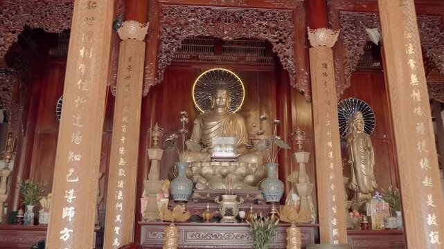 An altar with gilded bronze statue of Buddha Shakyamuni sitting in the meditation posture with vases and lotus flowers in front of the altar. Hai Duc Buddhist Institute located on Trai Thuy Hill in Nh