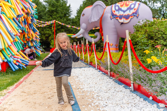 Excited little blonde girl fooling around and laughing at the striped canopy amusement park in an outdoor park