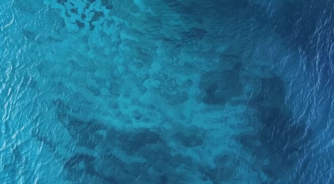 Aerial view of clear tropical ocean showing turquoise shallow reef, deeper blue water and gentle ripples across a sunlit sea