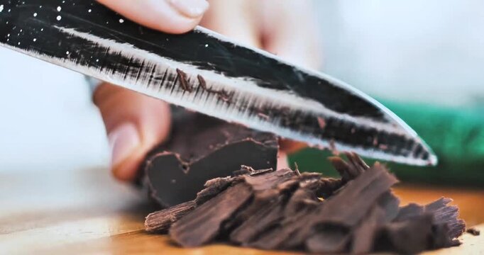 Close-Up of Chef Shaving Rich Dark Chocolate with a Sharp Knife on a Wooden Cutting Board for Dessert Decoration
