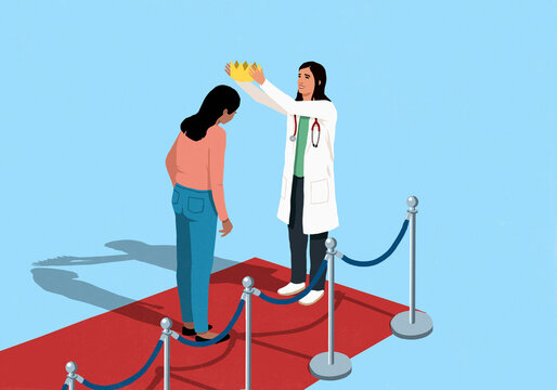 Female doctor placing crown on head of young woman standing on red carpet