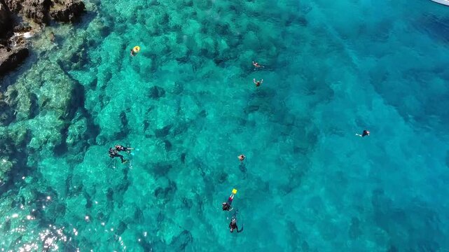 Aerial scuba diving training above rocky reef shows students and instructors in clear blue sea.
