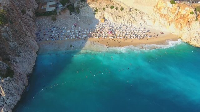 Aerial Kaputas Beach in Kas Antalya Turkey shows turquoise water, cliffs, umbrellas, and crowds.