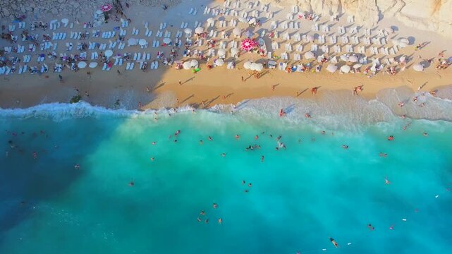 Aerial Kaputas Beach in Kas Antalya Turkey shows turquoise water, cliffs, umbrellas, and crowds.