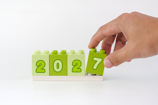 Hand placing the final 2027 number block on white background, representing preparation, change, planning and a new beginning.