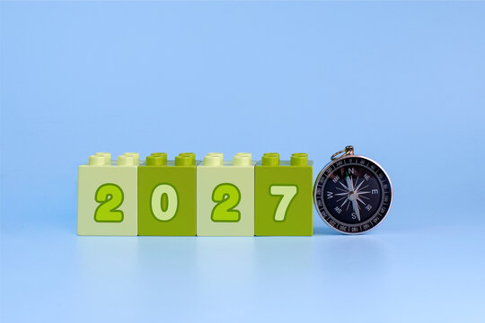 Green 2027 number blocks beside a compass on blue background representing direction, planning, goals and decisions for the new year.
