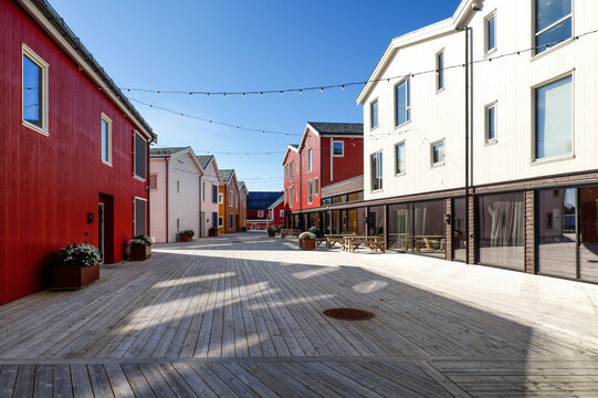 Traditional red and white wooden houses line a quiet street in Henningsv&aelig;r on the Lofoten Islands, with wooden paving, seating and blue sky on a sunny autumn day.