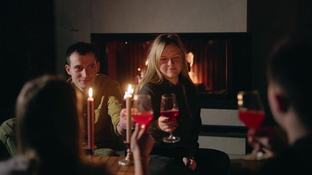 Friends Raise Wine Glasses Beside Fireplace at Candlelit Winter Gathering