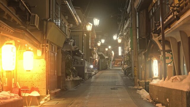 提灯の温かい明かりが灯る雪の温泉街の夜の石畳スローモーション
